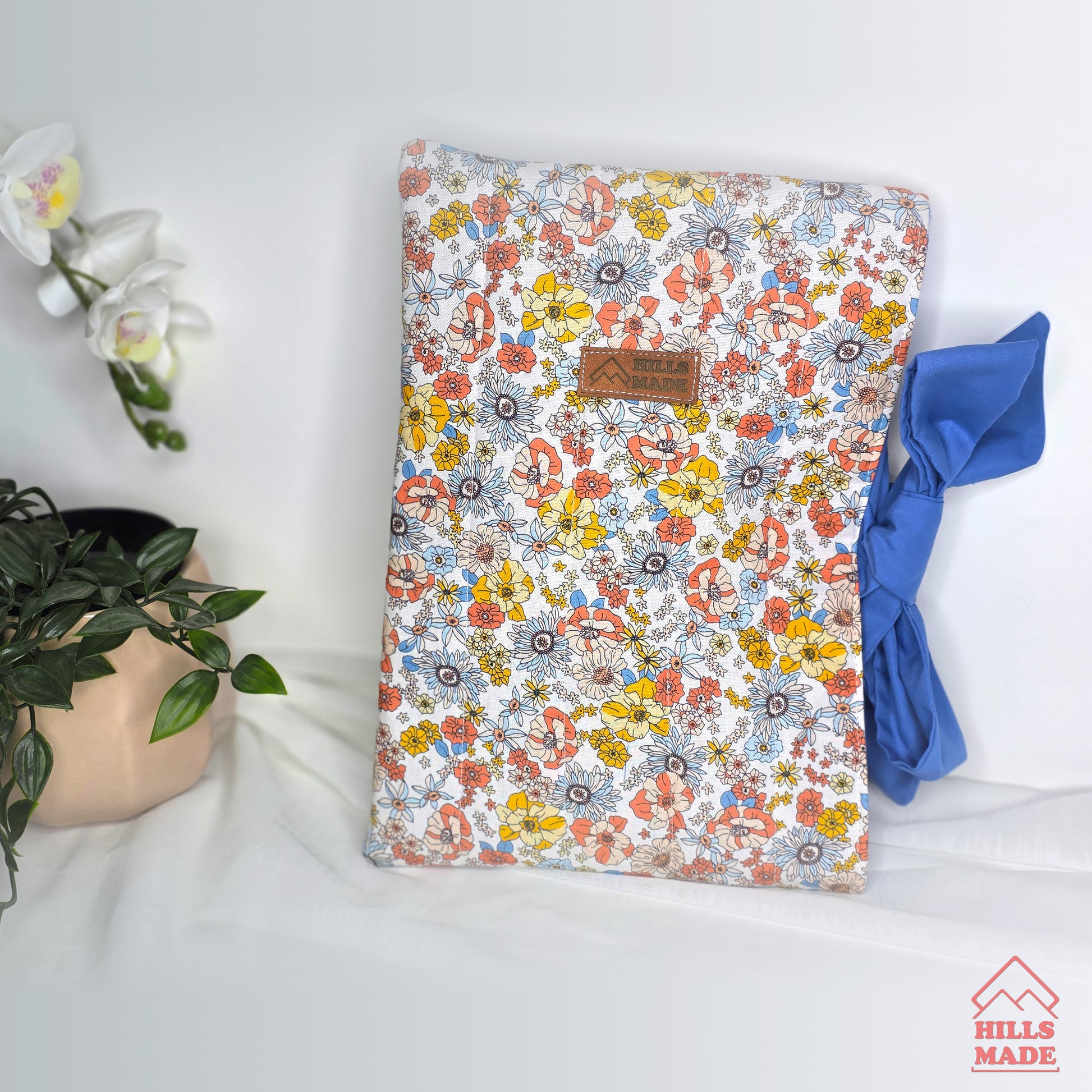 Floral-patterned book  sleeve with a plant and blue fabric on a white surface